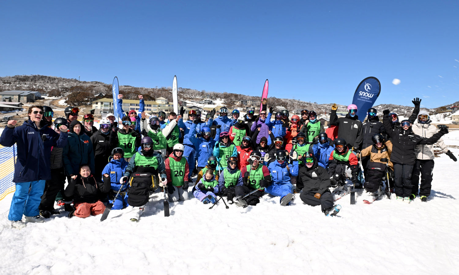 Group of people in winter sports gear posing on a snowy slope with a blue sky.