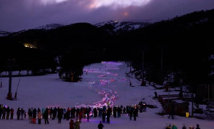 People gathered in a snowy landscape at night with illuminated pathways.