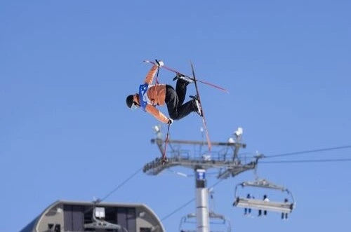 Person skiing in mid-air above ski lift infrastructure against a clear blue sky