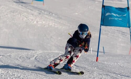 Skier in action on a snowy slope with a blue gate and 'Perisher' branding.