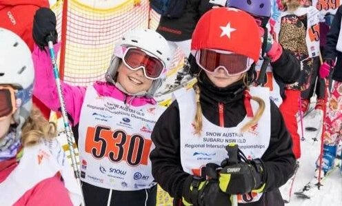 Two skiers in racing gear with bib numbers on a snowy background