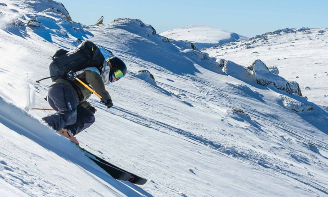 Person skiing down a snowy mountain with clear blue sky